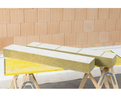 Mineralwolle-Dämmplatten mit weißer Beschichtung auf Arbeitsböcken vor einer Ziegelwand.