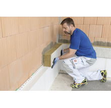 Ein Handwerker bringt Mineralwolle-Dämmplatten an einer Ziegelwand an, um eine fachgerechte Wärmedämmung im Innenbereich zu realisieren.