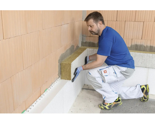 Ein Handwerker bringt Mineralwolle-Dämmplatten an einer Ziegelwand an, um eine fachgerechte Wärmedämmung im Innenbereich zu realisieren.