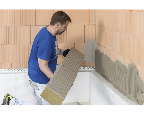 Handwerker bringt Steinwolle-Dämmplatte mit Klebemörtel an eine Ziegelwand zur Fassadendämmung an.