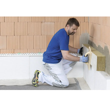 Ein Handwerker bringt Mineralwolle-Dämmplatten an eine Ziegelwand an.