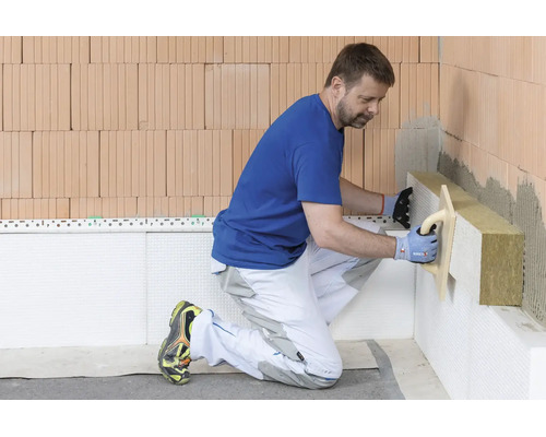 Ein Handwerker bringt Mineralwolle-Dämmplatten an eine Ziegelwand an.