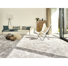 Heller Wohnraum mit Teppich, Sofa, Sessel und Holzelementen.