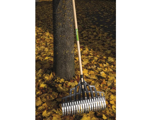 Laubbesen aus Kunststoff mit Holzstiel steht an einem Baum inmitten von Herbstlaub.