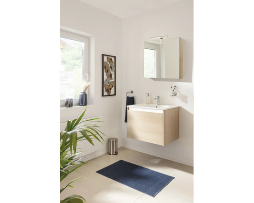 Modernes, helles Bad mit wandhängendem Waschtisch in heller Holzoptik, weißem Waschbecken, Spiegelschrank, Armatur und blauem Badeteppich.