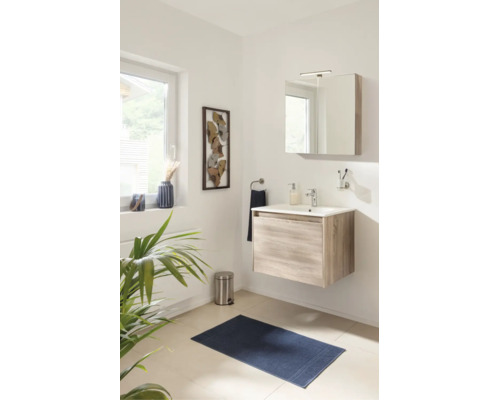 Helles Badezimmer mit wandhängendem Waschtischunterschrank in Holzoptik, weißem Waschbecken, Spiegelschrank, blauer Badematte und Dekoration.