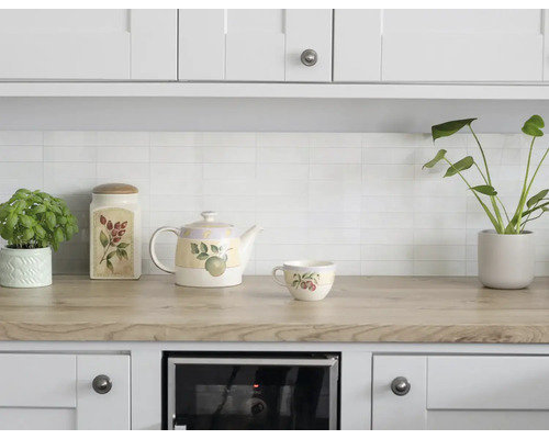 Helle Küchenzeile mit Arbeitsplatte in Holzoptik, weißen Wandfliesen, Teekanne, Tasse und Vorratsdose aus Keramik mit Pflanzenmotiven.