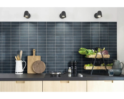 Moderne Küche mit dunklem Fliesenspiegel, hellen Holzschränken und Küchenutensilien unter drei Wandstrahlern.