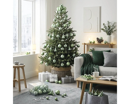 Hell dekorierter Wohnraum mit Weihnachtsbaum in einem Weidenkorb, geschmückt mit Kugeln. Daneben Sofa, Couchtisch und Geschenke.