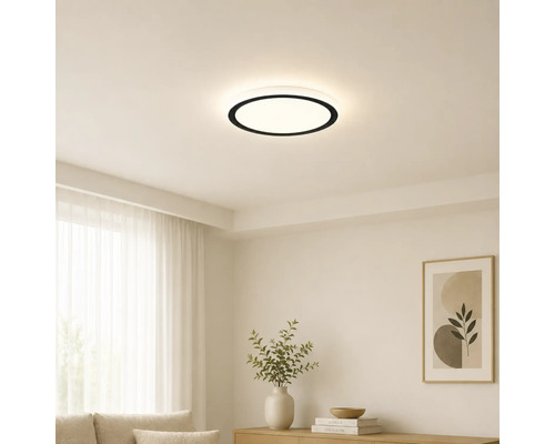 Moderne runde LED-Deckenleuchte mit schwarzem Rand in einem hellen, minimalistischen Wohnzimmer mit weißen Wänden und hellen Möbeln.