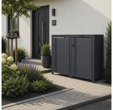 Moderne Mülltonnenbox aus Metall für zwei Tonnen im Vorgarten mit gepflastertem Weg und Pflanzen neben einem Hauseingang.