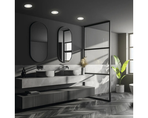 Modernes Badezimmer mit Doppelwaschtisch aus Stein und runden Spiegeln, beleuchtet durch integrierte Deckeneinbaustrahler.
