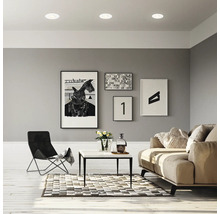 Ein modern eingerichtetes Wohnzimmer mit LED Einbauleuchten, einem Sofa, einem Sessel, einem Beistelltisch und Wandbildern.