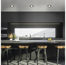 Moderne Küche mit dunkler Küchenzeile, Arbeitsplatte, Barhockern aus Holz und drei runden Deckenleuchten in einer minimalistischen Umgebung.