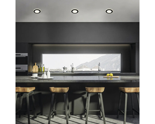 Moderne Küche mit dunkler Küchenzeile, Arbeitsplatte, Barhockern aus Holz und drei runden Deckenleuchten in einer minimalistischen Umgebung.