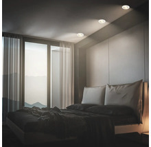 Modernes Schlafzimmer mit Einbaustrahlern an der Decke neben einem Fenster mit bodentiefen Vorhängen und einem Doppelbett.