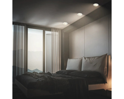 Modernes Schlafzimmer mit Einbaustrahlern an der Decke neben einem Fenster mit bodentiefen Vorhängen und einem Doppelbett.