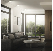 Modernes Wohnzimmer mit Einbaustrahler an der Decke, Sofa, Couchtisch aus Stein und bodentiefen Fenstern mit Gartenblick.