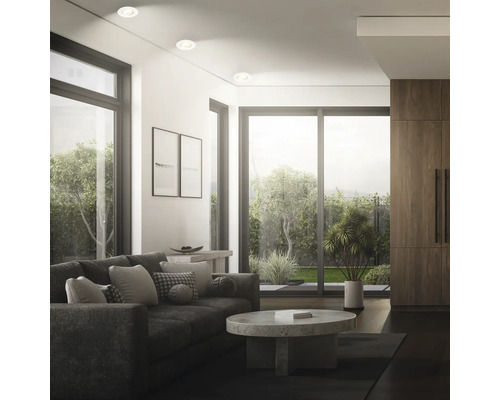Modernes Wohnzimmer mit Einbaustrahler an der Decke, Sofa, Couchtisch aus Stein und bodentiefen Fenstern mit Gartenblick.