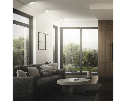Modernes Wohnzimmer mit Einbaustrahlern in der Decke, bodentiefen Fenstern, bequemen Sofa und Couchtisch mit Blick in den Garten.