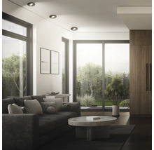 Modernes Wohnzimmer mit Einbaustrahlern an der Decke, Sofa, Couchtisch aus Stein und bodentiefen Fenstern mit Blick auf den Garten.