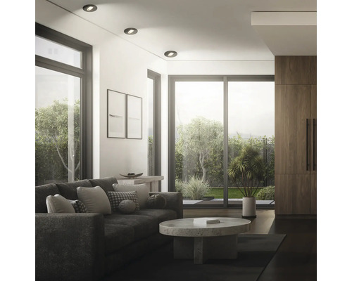 Modernes Wohnzimmer mit Einbaustrahlern an der Decke, Sofa, Couchtisch aus Stein und bodentiefen Fenstern mit Blick auf den Garten.