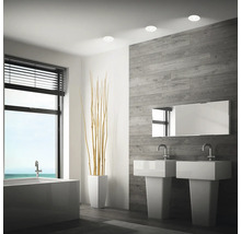 Modernes Badezimmer mit zwei Waschbecken, Badewanne, Wandverkleidung in Holzoptik und Einbaustrahlern an der Decke.