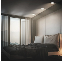 Modernes Schlafzimmer mit Einbaustrahlern in der Decke über einem Doppelbett vor einer großen Fensterfront mit Blick auf Berge.