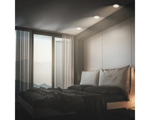 Modernes Schlafzimmer mit Einbaustrahlern in der Decke über einem Doppelbett vor einer großen Fensterfront mit Blick auf Berge.