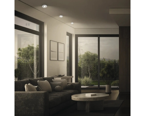 Modernes Wohnzimmer mit Einbaustrahlern an der Decke, dunklem Sofa und großem Fenster mit Blick in den Garten.