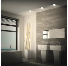 Modernes Badezimmer mit zwei Standwaschbecken, Spiegel und Einbaustrahlern an der Decke vor einer Wand mit Holzoptik Fliesen.