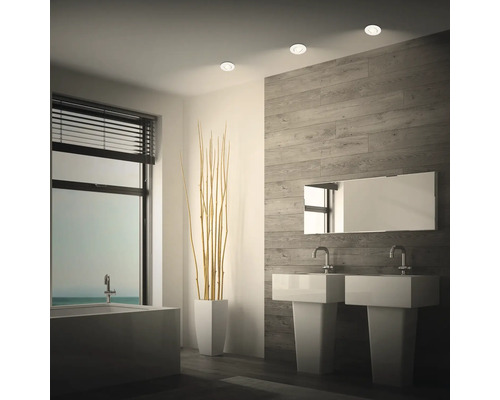 Modernes Badezimmer mit zwei Standwaschbecken, Spiegel und Einbaustrahlern an der Decke vor einer Wand mit Holzoptik Fliesen.