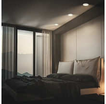 Modernes Schlafzimmer mit drei runden Deckeneinbaustrahlern, die den Raum in ein atmosphärisches Licht tauchen, mit Blick auf eine Gebirgslandschaft.