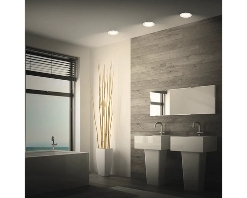 Modernes Badezimmer mit Doppelwaschbecken, Badewanne, holzoptischer Wandverkleidung und drei runden Deckenstrahlern für indirekte Beleuchtung.