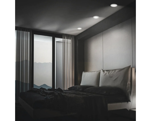 Modernes Schlafzimmer mit Einbauleuchten an der Decke, bodentiefem Fenster und minimalistischem Bett vor einer Wandverkleidung.