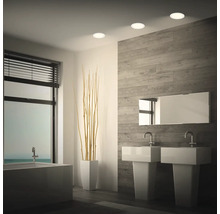 Modernes Badezimmer mit Deckeneinbauleuchten, zwei Waschbecken, Badewanne und Wandverkleidung in Holzoptik.