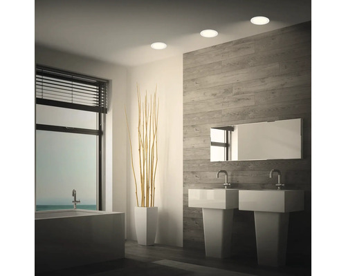 Modernes Badezimmer mit Deckeneinbauleuchten, zwei Waschbecken, Badewanne und Wandverkleidung in Holzoptik.