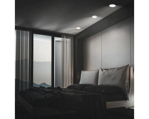 Modernes Schlafzimmer mit Einbaustrahlern in der Decke, bodentiefen Fenstern und Blick auf Berge bei Dämmerung.