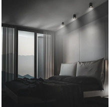 Modernes Schlafzimmer mit minimalistischem Design und drei zylindrischen Deckenstrahlern, die das Kopfteil des Bettes akzentuieren.