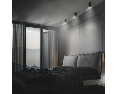 Modernes Schlafzimmer mit minimalistischem Design und drei zylindrischen Deckenstrahlern, die das Kopfteil des Bettes akzentuieren.