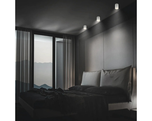 Modernes Schlafzimmer mit drei zylindrischen LED Deckenstrahlern, die für eine dezente Akzentbeleuchtung an der Wand über dem Bett sorgen.