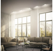 Helles, modern eingerichtetes Wohnzimmer mit eingebauten Deckenstrahlern, großen Fenstern und gemütlichen Sofas.
