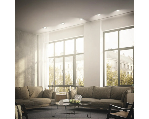 Helles, modern eingerichtetes Wohnzimmer mit eingebauten Deckenstrahlern, großen Fenstern und gemütlichen Sofas.