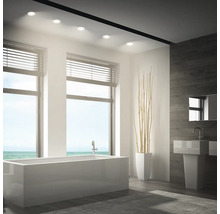 Modernes Badezimmer mit integrierten Deckeneinbaustrahlern, Badewanne, Waschbecken und Holzoptikwand.