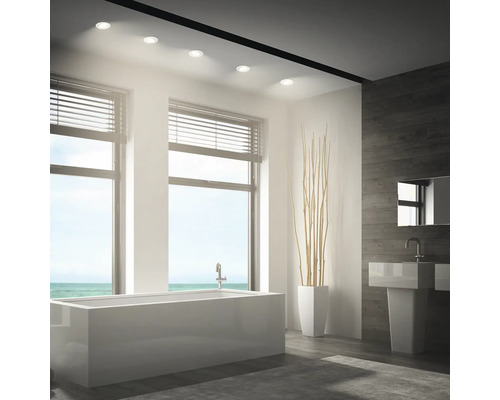 Modernes Badezimmer mit integrierten Deckeneinbaustrahlern, Badewanne, Waschbecken und Holzoptikwand.