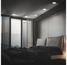 Modernes Schlafzimmer mit Einbaustrahlern an der Decke und Blick auf eine Berglandschaft durch ein großes Fenster mit Vorhängen.
