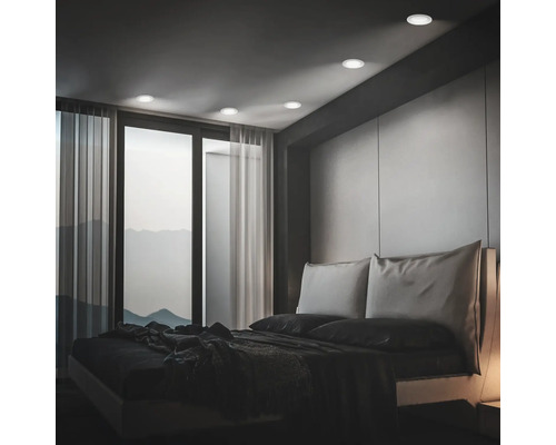 Modernes Schlafzimmer mit Einbaustrahlern an der Decke und Blick auf eine Berglandschaft durch ein großes Fenster mit Vorhängen.