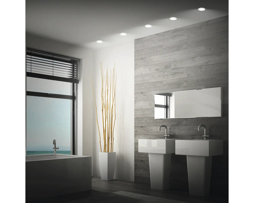 Modernes Badezimmer mit zwei Standwaschbecken, Spiegel und Einbaustrahlern an einer holzoptik gefliesten Wand vor einem Fenster mit Jalousien.