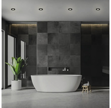 Modernes Badezimmer mit freistehender weißer Badewanne vor dunkler Fliesenwand, Einbaustrahlern in der Decke und einer grünen Zimmerpflanze.