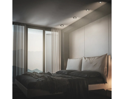Modernes Schlafzimmer mit Einbaustrahlern in der Decke, großem Bett und bodentiefem Fenster mit Vorhängen.